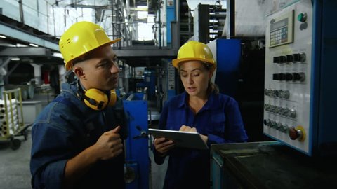 Zoom out shot of mature woman showing factory machine to male employee and explaining how to operate it