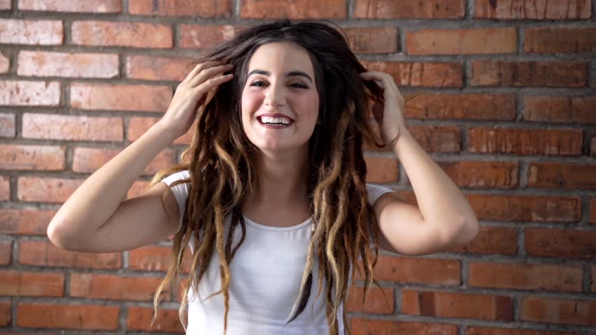 portrait of young beautiful woman with dreadlock on her hair standing against brick wall