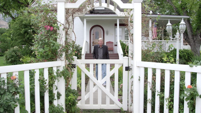 Elderly man walking with a cane as he opens and closes the gate in his yard.