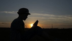 silhouette of a boy uses a tablet at sunset in the field, reads something on the tablet