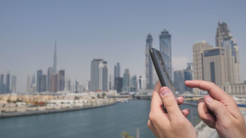 A man texts a message on the phone in the background of the panorama of Dubai. Hand close-up.