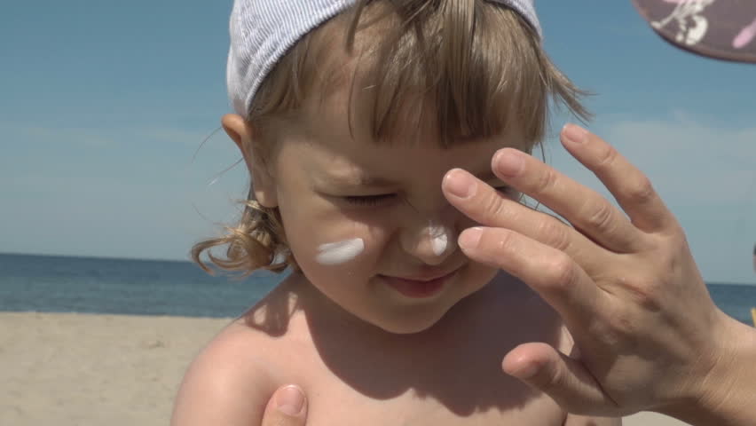 Sun protection. Mother anoints her son face protective cream on the beach. Family vacation at the sea. Slow motion.  Portrait of little boy in suncream | Shutterstock HD Video #1017084496