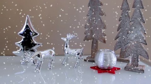 Christmas decoration with toy deers, fir- trees and decorative candle and snow standing on a white sideboard. Slow motion