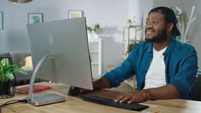 Portrait of the Stylish African American Working on a Personal Computer while Sitting at His Desk at Home. Shot on RED EPIC-W 8K Helium Cinema Camera.