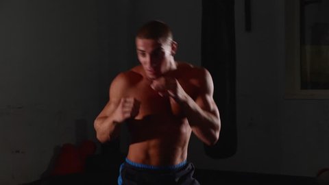 Male muscular topless boxer exercising shadow boxing. Fighter training punching in the darknes in slow motion.