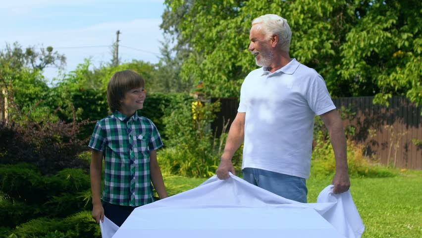 Grandpa and grandson spreading white table cloth, giving high five to each other