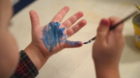 Funny child paints his hands with paint. Baby artist.