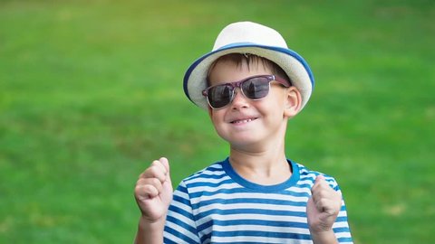 Portrait happy smiling little boy in sunglasses and hat having fun dancing in summer park