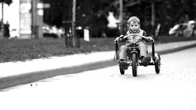 Happy child on bike having fun outdoors. Active kid boy riding retro stylish bicycle. Cute little boy playing and cycling on street road and spending family time. Slow motion black and white.