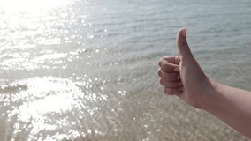 Female manicured hand with thumb up gesture isolated at sunny morning calm sea background. Real time full hd video footage with copyspace.