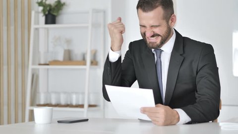 Businessman Celebrating Success while Reading Documents in Office