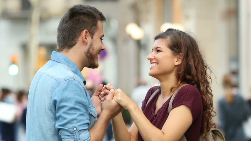 Side view of a happy couple flirting holding hands and hugging in the street