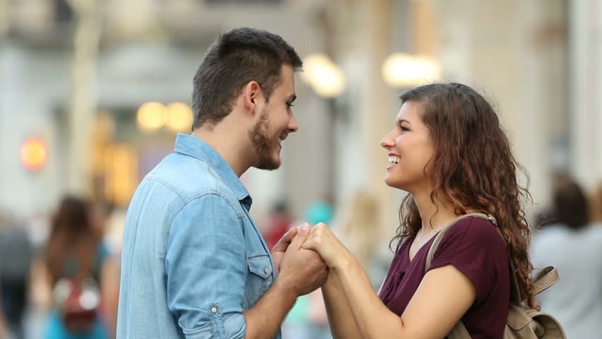 Side view of a happy couple flirting holding hands in the street