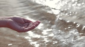 Closeup view of one female hand holding clear water outdoors on sandy tropical sea water background. Happy summer holidays and vacations at hotel resort. Real time full hd video footage.