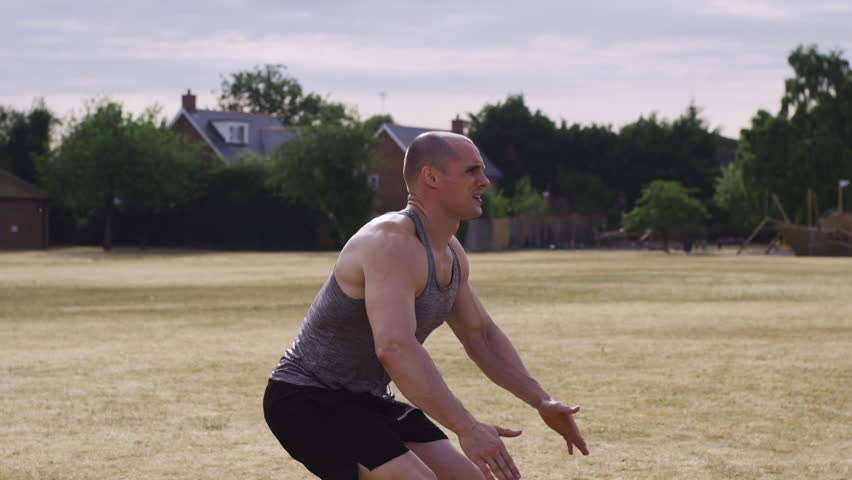 Athletic muscular guy exercising outside doing jump squats