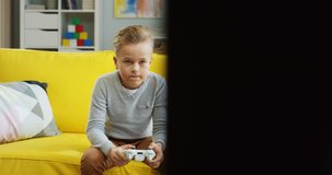 Cheerful Caucasian small boy playing videogames with a joystick in hands and being excited.