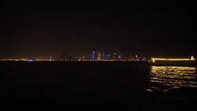 Single boat crosses the dramatic cityscape of Doha. Qatar at night. with its lights reflecting on the surface of the bay. Video 4k Ultra HD