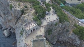 Shooting from the air of architectural landmark castle Swallows nest in Gaspra, Yalta region, Crimea. Tourists walking on the pier to get on a ship for sea excursion. Beautiful coast with beach, trees