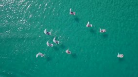 Aerial footage of a Group of small sail boats led by a small rubber boat, manoeuvring in the calm waters of a Mediterranean bay