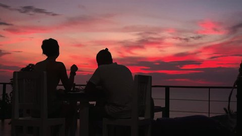 Romantic couple dinner in viewpoint restaurant with amazing colorful sunset on background