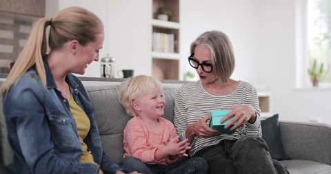 Boy opening a birthday present with grandmother and mother