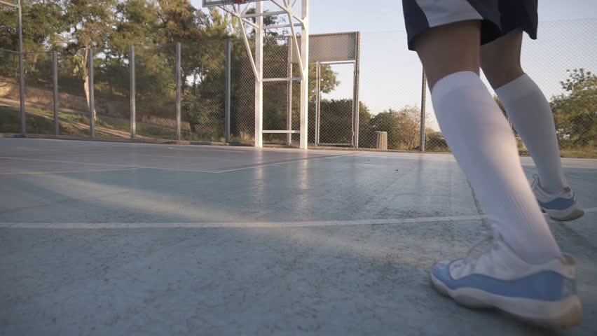 Low angle footage of a proffesional female basketball player in action. Girl's practicing outdoors on the court, throwing a ball to the net. Backside view