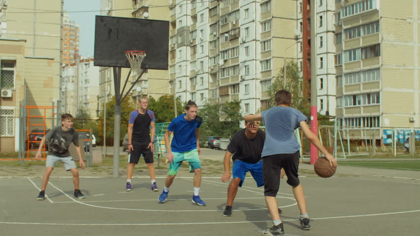 Teenage basketball forward setting a screen on defender and receiving a pass from teammate, taking easy layup shot during streetball game. Streetball team making successful pick and roll play on court Royalty-Free Stock Footage #1017166078