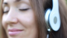 Woman listening to music in headphones with eyes closed on the outdoor. Portrait of a beautiful girl closeup