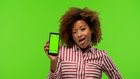 Afro american woman holding phone on green chroma winking, funny joke, symbol of agreement or complicity