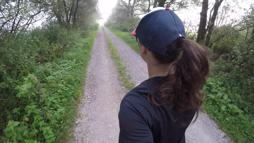 Woman running on a trail road, wearing baseball cap. 4K video.