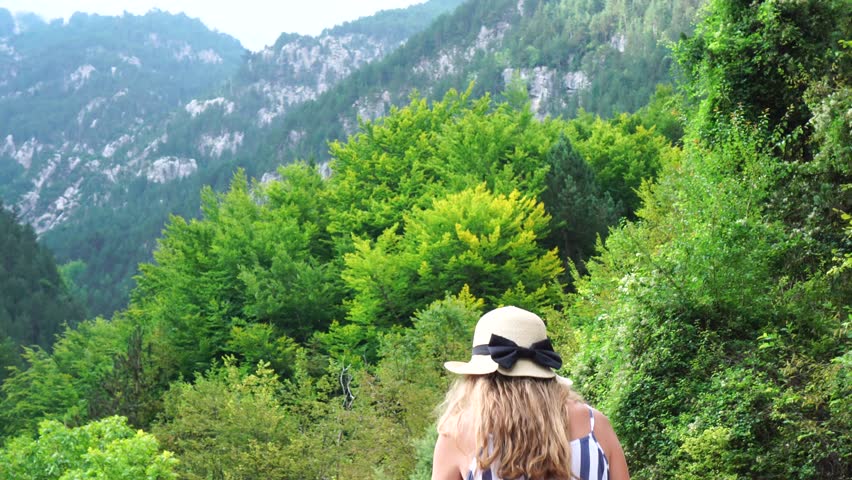 Blond hair young woman in stripped clothes and straw hat wandering around pine tree forest on top of Olympus mountain