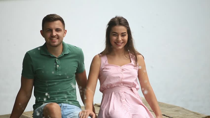 Beautiful youn couple sit on the pier near the lake. make splash by feet. slow motion