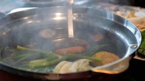 Suki or Shabu boiling in electric pot with turnips, morning glory, pork chops, squid, corn, vermicelli and pork. video Slow motion