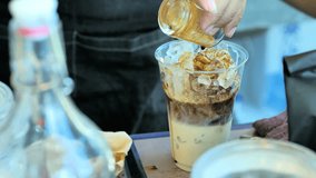 Professional barista pouring coffee into a glass with ice and adding milk in a busy coffee shop. Video Slow Motion