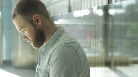 Lonely disappointed bearded guy leaning on glass wall, receiving bad information