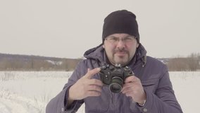 A man takes a picture. shoots on an old camera. Winter season. Warm clothing. Snow field. Bright day. Largest species. 4K video