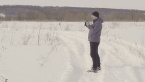 A man takes pictures in the field. Winter season. Warm clothing. Much snow. Full growth. Bright day. View to the waist. 4K video
