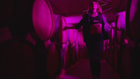 Hot girl dancing . Dances with real strobe lights in colorful light winery with brandy , whiskey or wine barrels . Sexy body posing in wine house . 