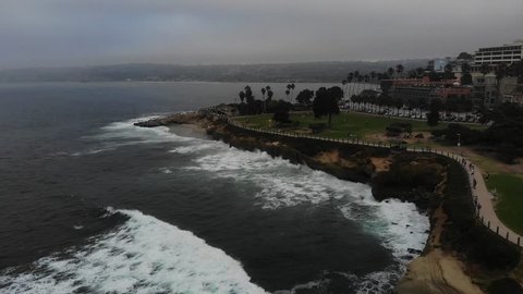 Seascape Drone Views Facing California, La Jolla Coastline and Cove, People Walking Along Path, Waves Crashing Along Rocks, Cliff Side Houses In Background, Beverly Hills 