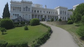 Shooting from the air of Livadiysky Palace, Yalta region. Tourists walking  cross the beautiful park of great conifers trees, posing, making photos. Aerial video of  South coast of Crimea.