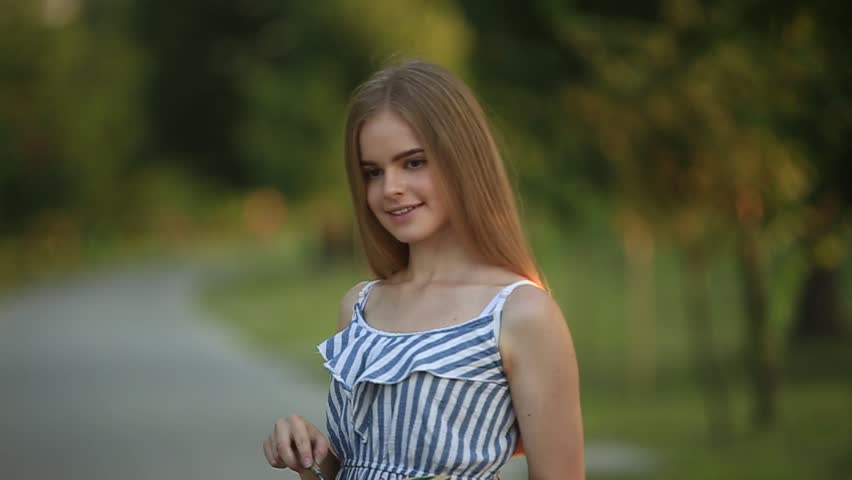 Beautiful girl draws a picture in the park using a palette with paints and a spatula. Easel and canvas with a picture. Summer is a sunny day, sunset.