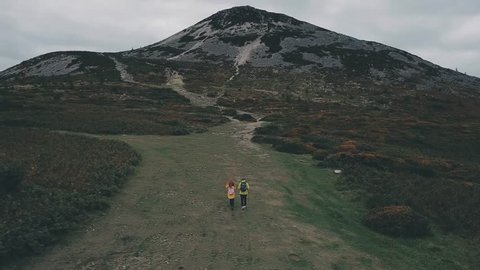Epic aerial 4k shot of couple in yelow jackets hiking in mountains in dark cloudy weather. Ireland, Wicklow mountains.