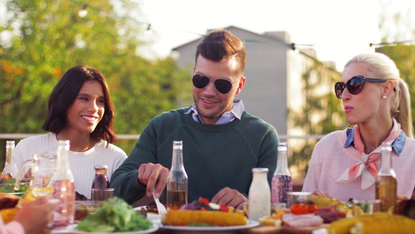 Leisure and people concept - happy friends eating at rooftop party in summer | Shutterstock HD Video #1017259333