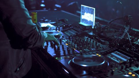 Dj mixes the track in the nightclub at party. Headphones in foreground and DJ hands in motion. Rave.