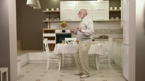 Cheerful Old Man Dancing In The Kitchen. Happy Grandpa