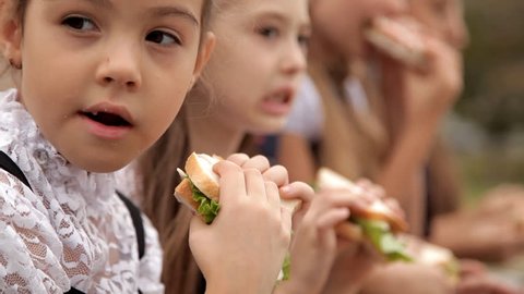 Children in school uniform after classes spend time in the park at the bottom of a sandwich. Delicious food, a sandwich day