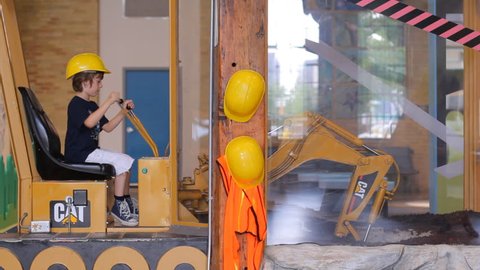 Boy in yellow builder helmet sitting in simulator of excavator and playing with joystick