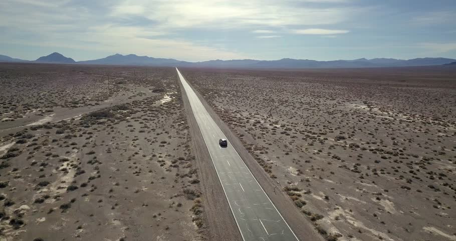 Incredible landscape of Death Valley with a highway on the background of the mountains and cloudy sky in Nevada, USA. Dark SUV car is moving on the road. Aerial video recording.