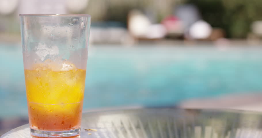 Tropical drink on table in front of pool - alcholic ice tea - picked up by womans hand