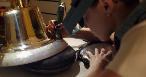 The engraver applies the inscription on the bell with the drill. Woman engraver,  engraving on the bell.